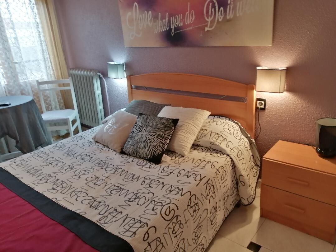 A neatly made bed with patterned bedding, a bedside table with a lamp, and a wall with a motivational quote.