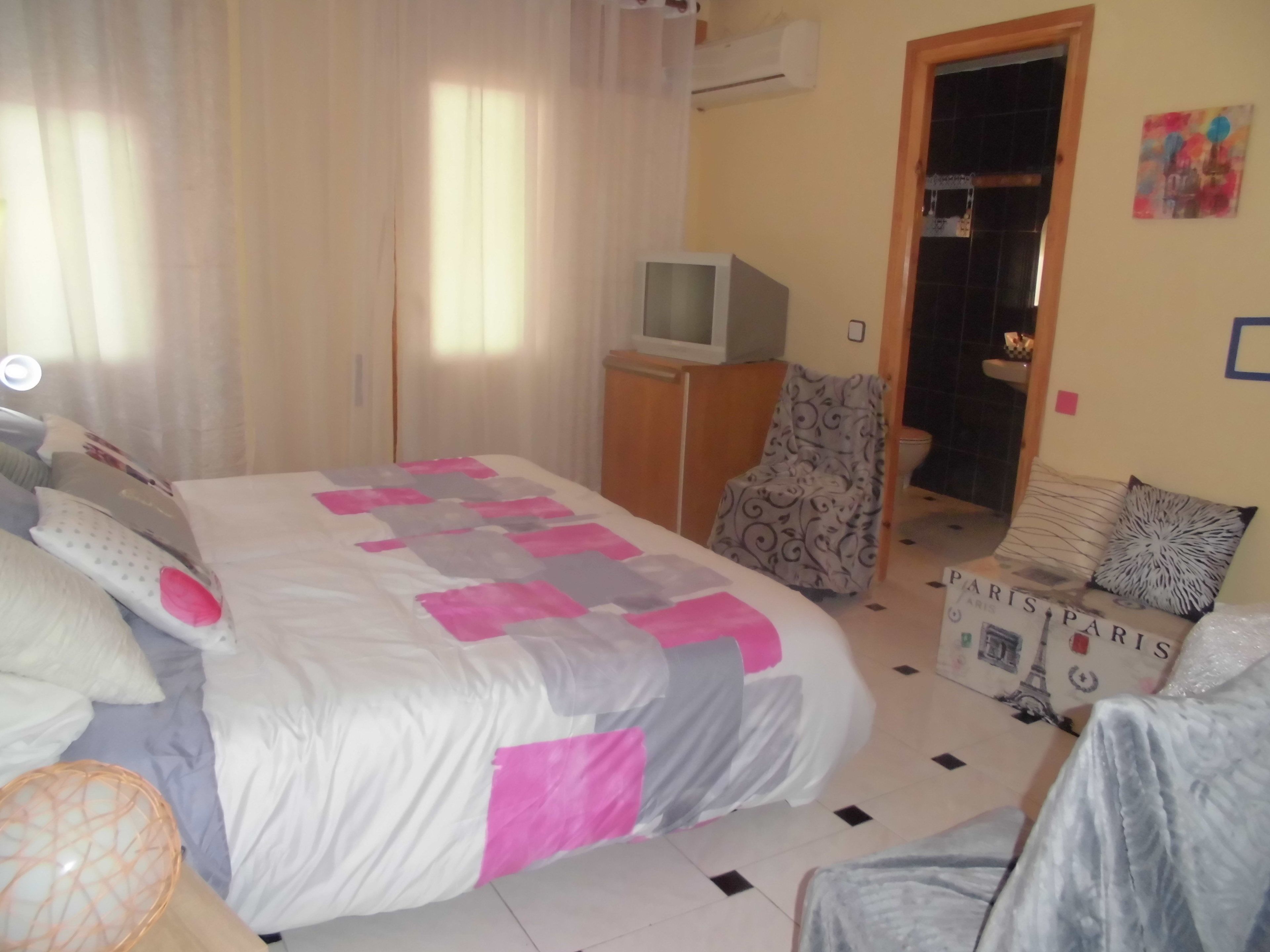 Un dormitorio con cama, una silla, un televisor y una puerta que da a un baño.