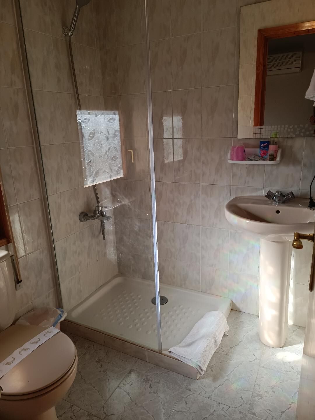 A bathroom with a glass-enclosed shower, a toilet, and a sink.