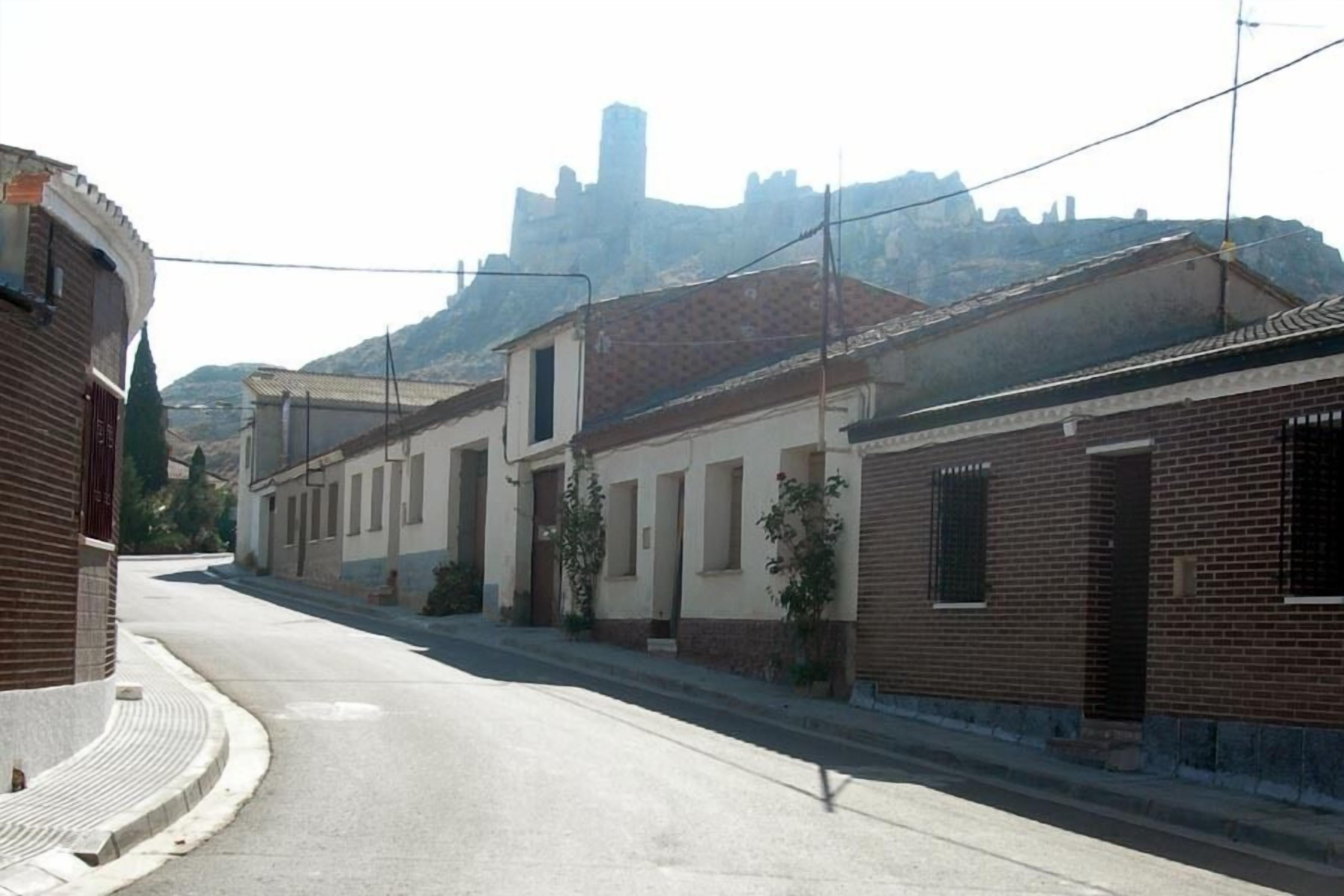 Une rue tranquille bordée de bâtiments traditionnels, un ciel dégagé et, au loin, une structure qui ressemble à un château.