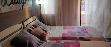 Un dormitorio con dos camas, un cabecero con un letrero que dice 'Laugh', una lámpara de noche y cortinas de voile.
