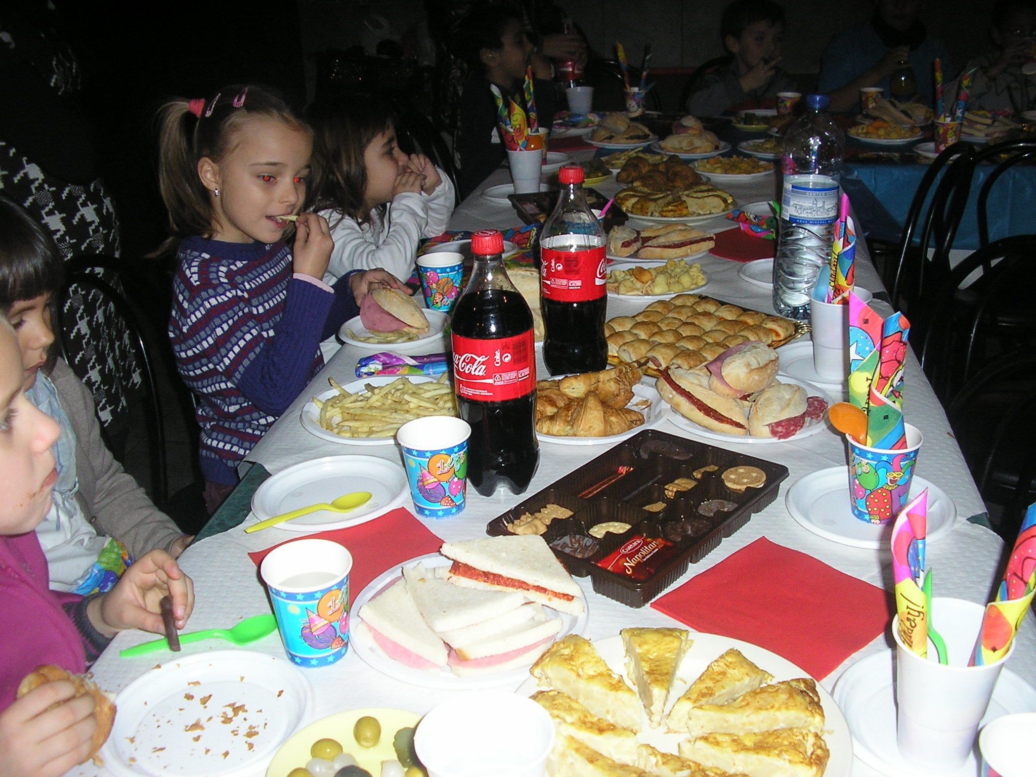 Una mesa de comedor con diversos alimentos y bebidas, como sándwiches, papas fritas y una botella de Coca-Cola.