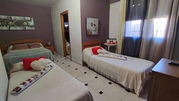 Habitación de hotel con dos camas individuales, una mesita, una silla, un escritorio y una ventana con cortinas.