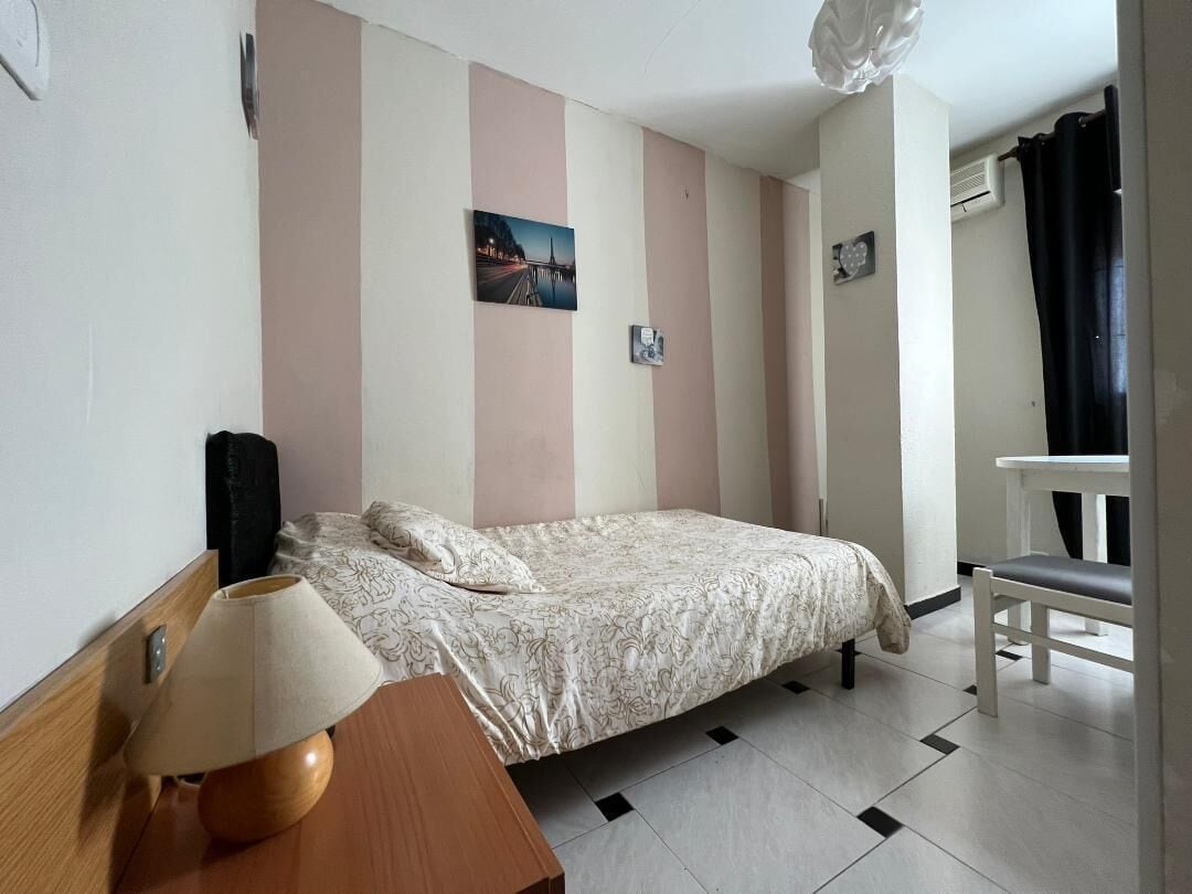 A bedroom with a bed, a bedside table, a lamp, and a chair.
