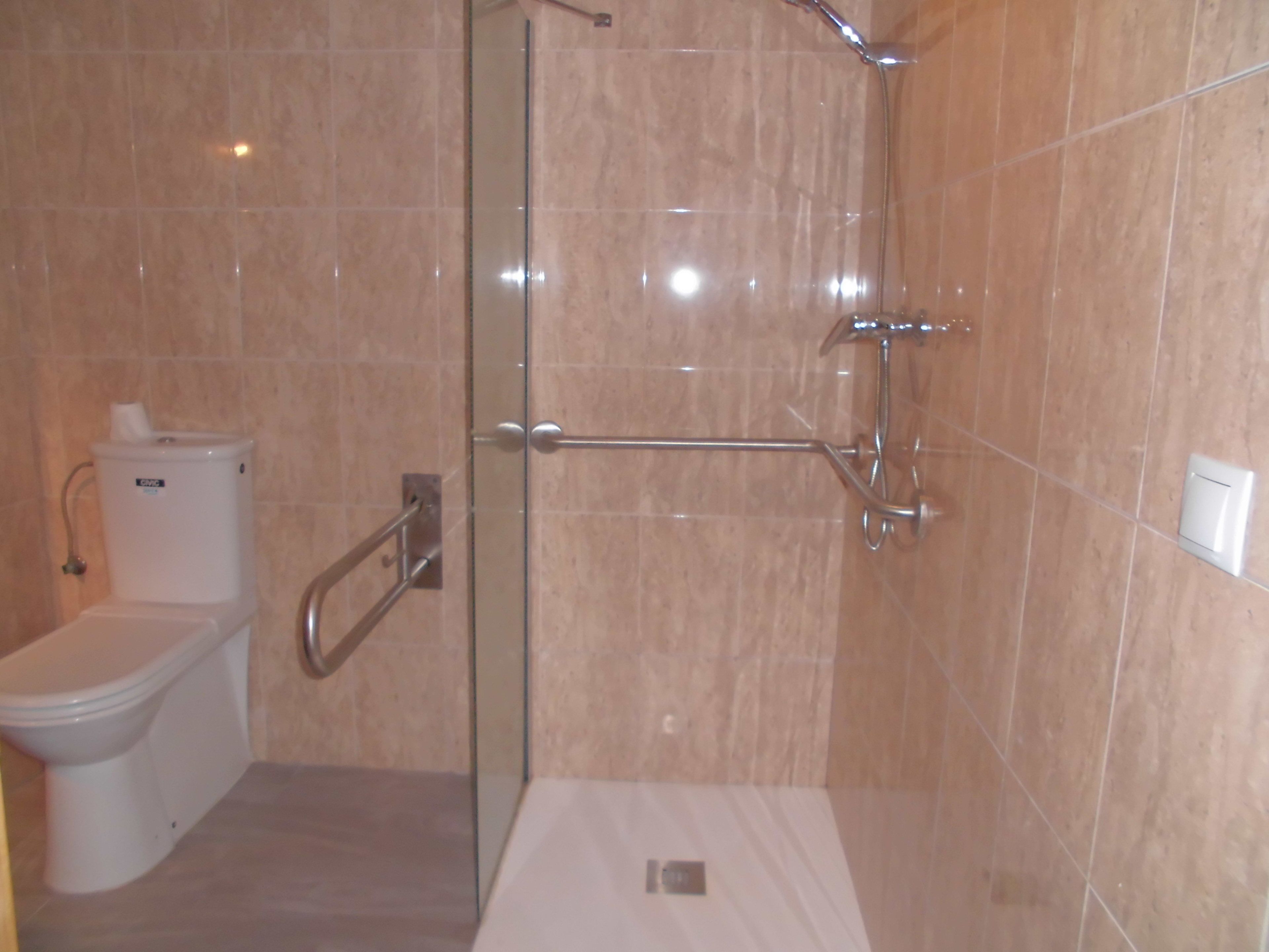 Un baño con inodoro, ducha y zona de ducha con mampara de vidrio.