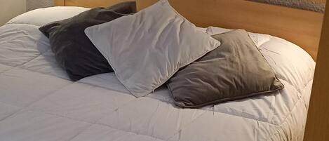 A bed with a white quilt and two pillows, one dark and one light.