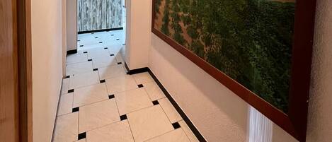 Un pasillo con suelo de baldosas, un cuadro grande enmarcado en la pared y una puerta a la izquierda.