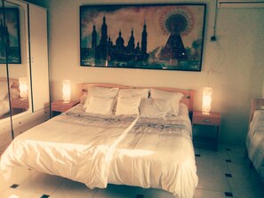 A neatly made bed with white linens in a hotel room, a large painting of a cityscape above the bed, and two bedside lamps on nightstands.