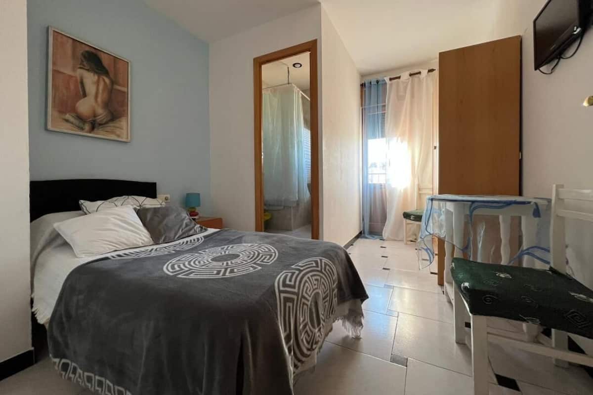 Een slaapkamer met een bed, een schilderij aan de muur, een televisie en een badkamer die door een open deur zichtbaar is.