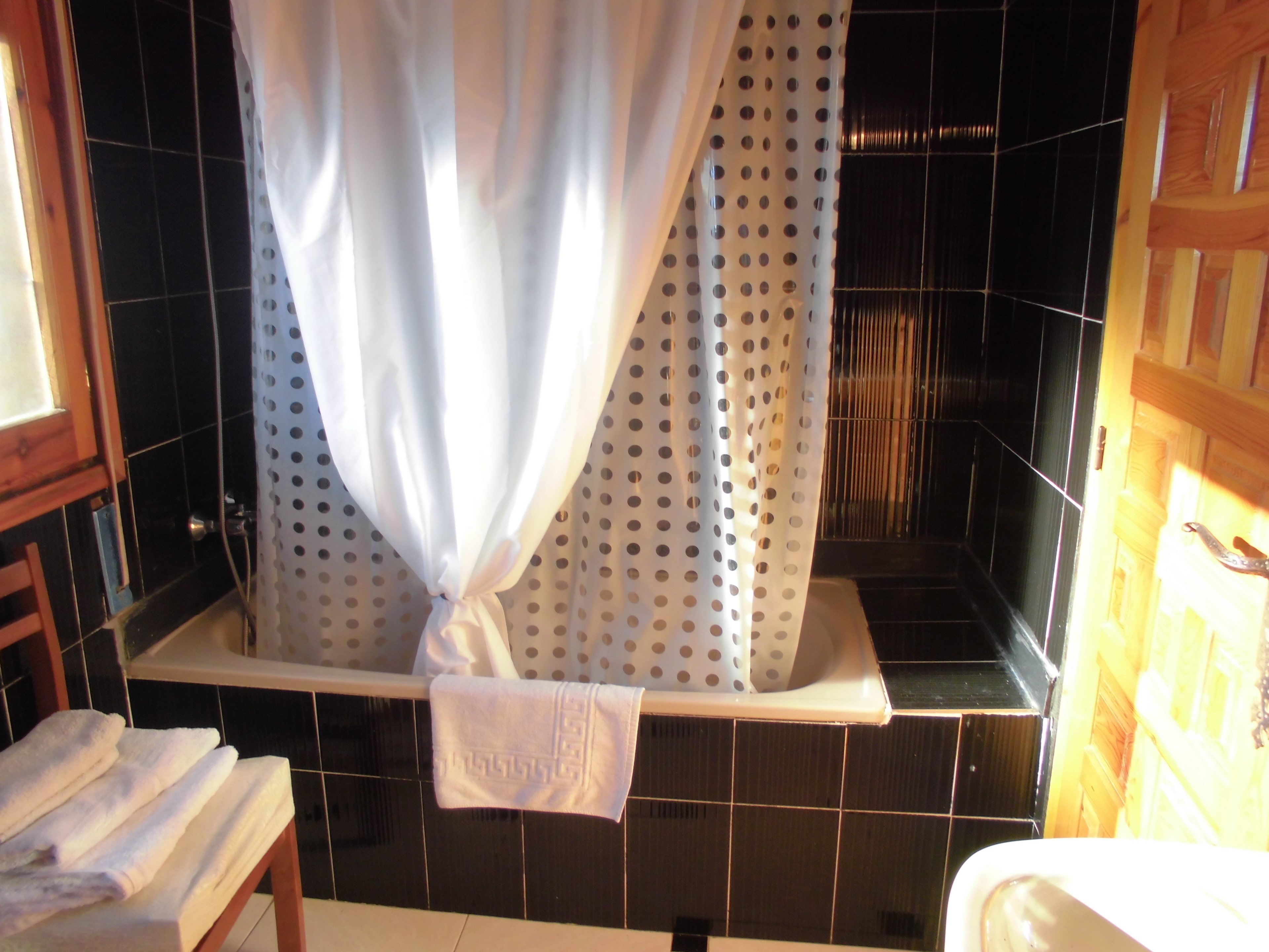 Un baño con bañera, un perchero con toallas y una cortina a lunares.