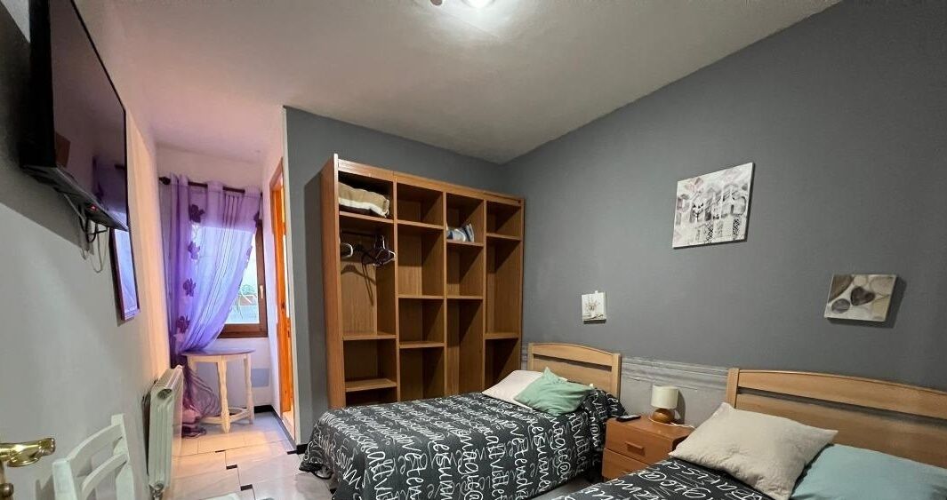 Un dormitorio con dos camas, un armario de madera, una mesita pequeña y un radiador.