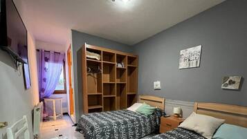 Un dormitorio con dos camas, un armario de madera, una mesita pequeña y un radiador.