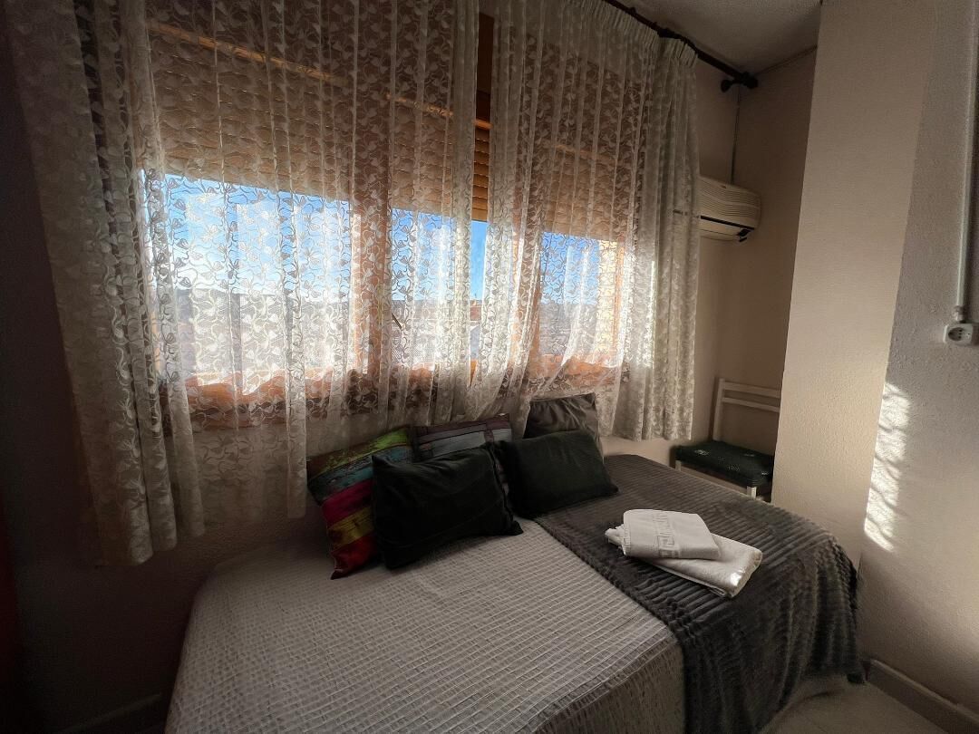 Ein Schlafzimmer mit einem Bett, Kissen, einer Decke und Spitzenvorhängen.