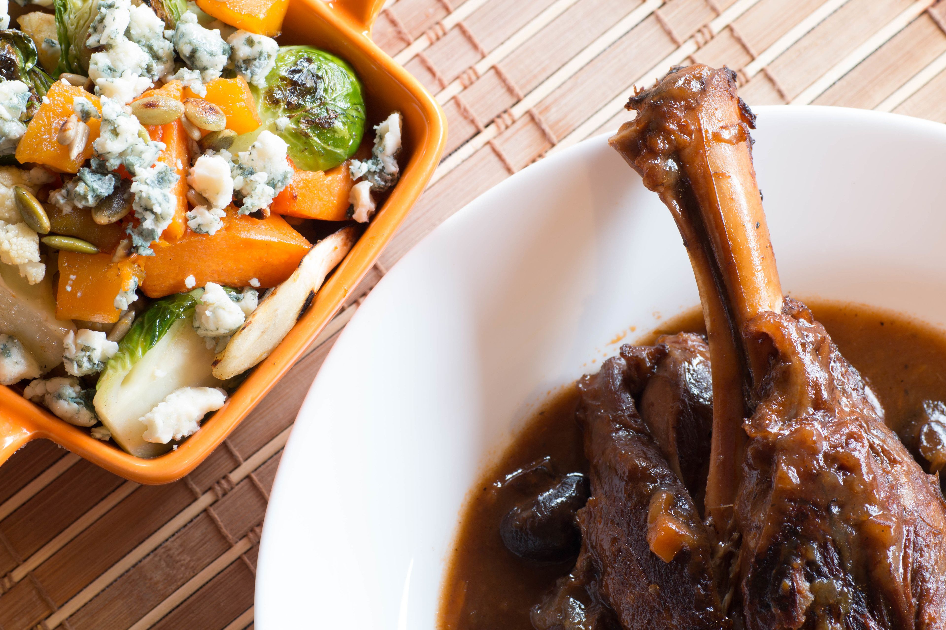 A meal with a roasted leg of lamb and a side of vegetables and blue cheese.