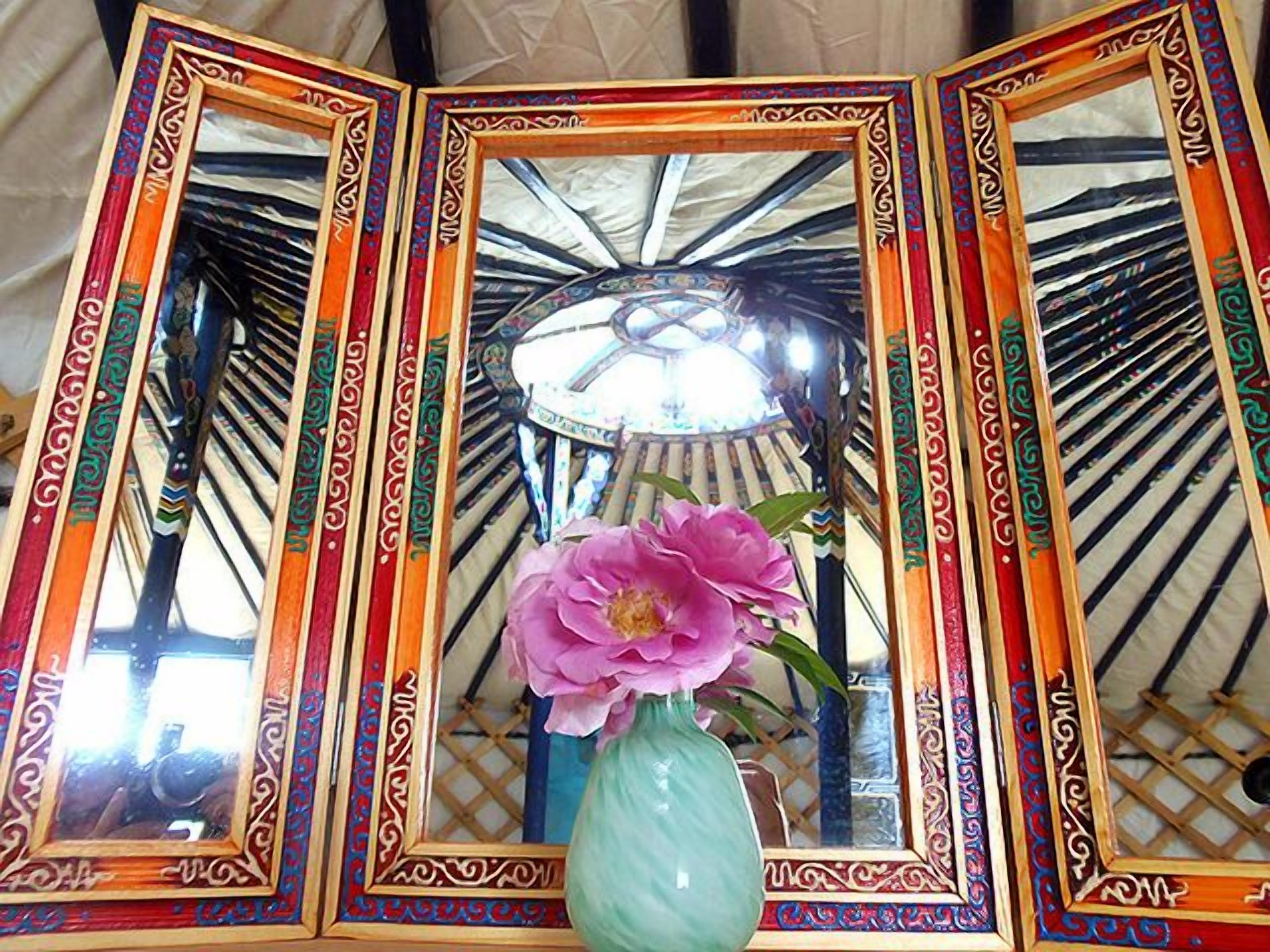 A room with a decorative mirror set and a vase with a flower.