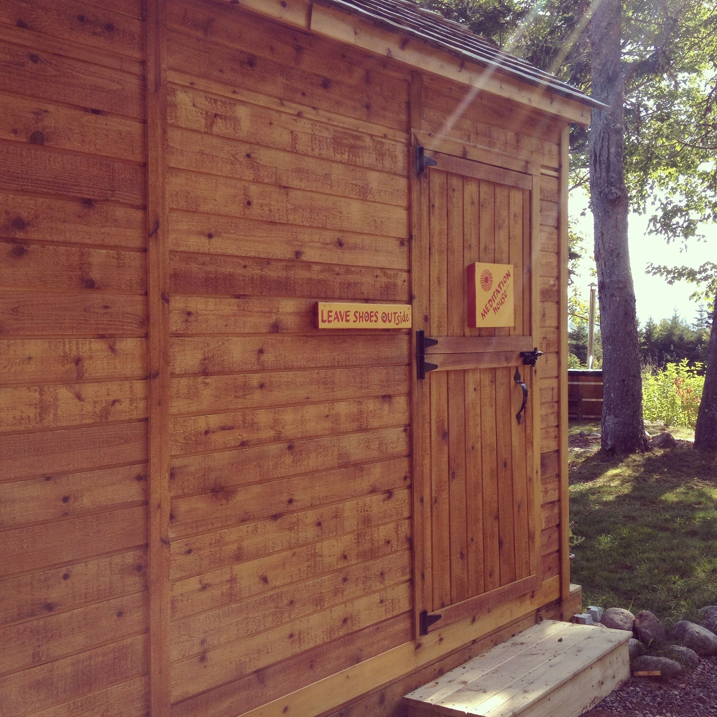 A wooden building with a sign that reads "Leave Shoes Outside" and another sign indicating a "Meditation House."