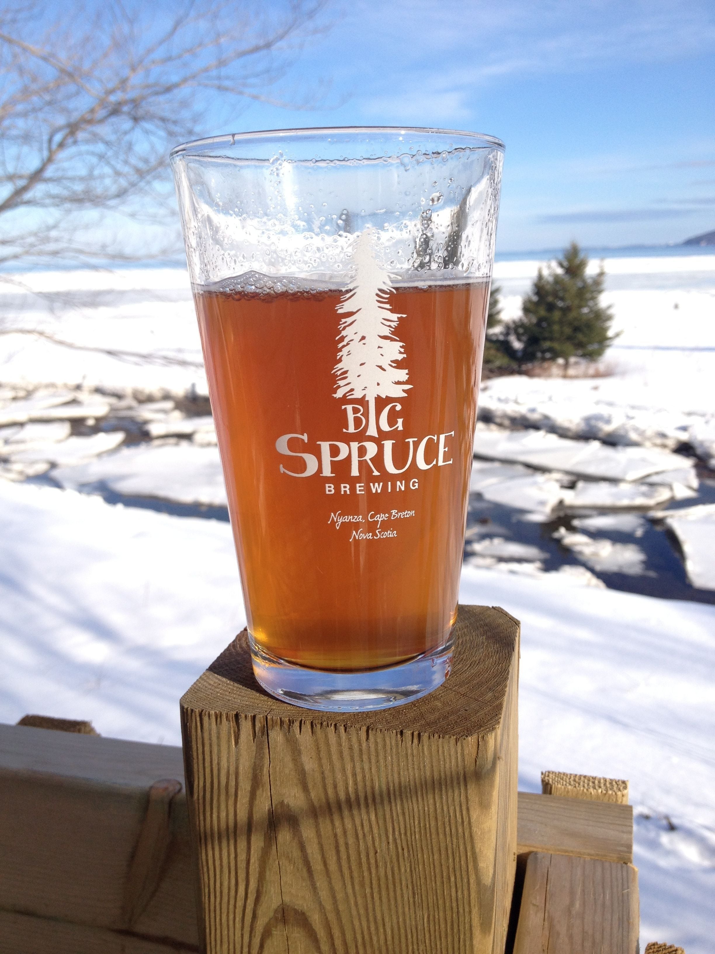 Un verre de bière avec le logo d’un arbre sur un poteau en bois, dans un paysage enneigé.