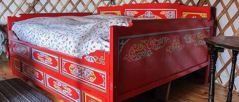 A red bed with intricate designs and a wooden floor.