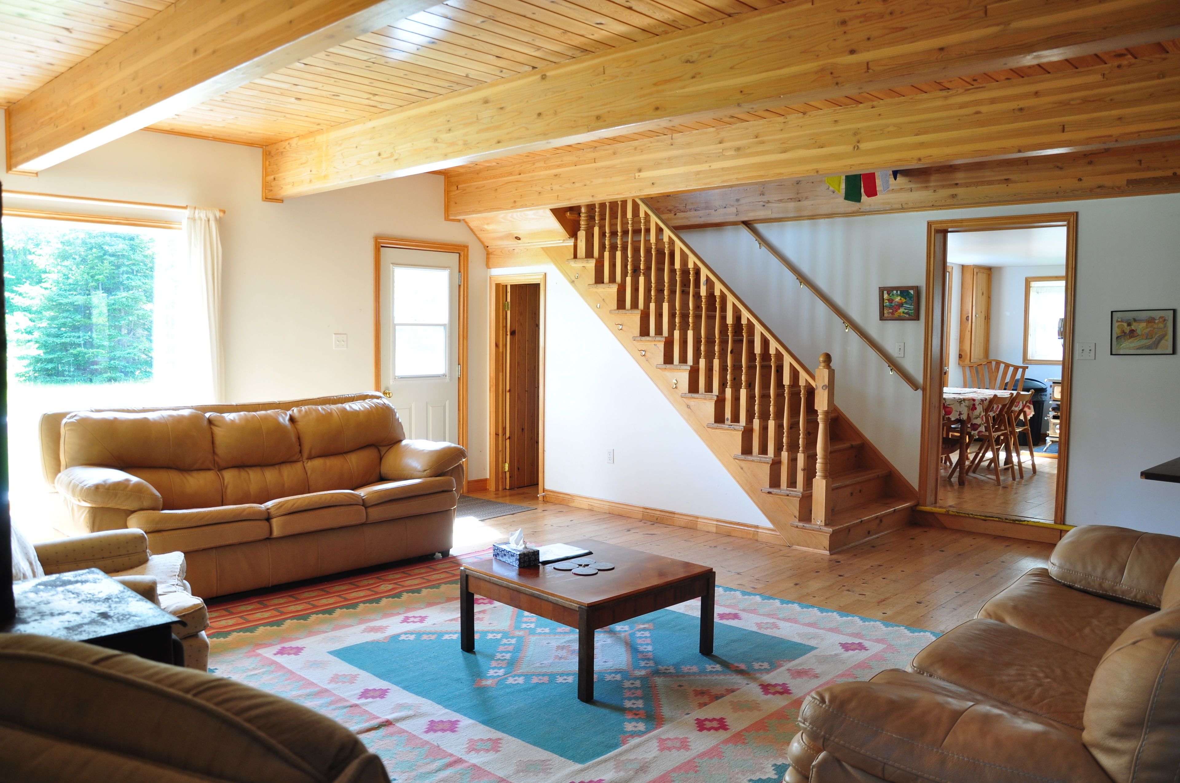 Un salón amplio con escalera de madera, un sofá de cuero marrón y una mesa de centro.