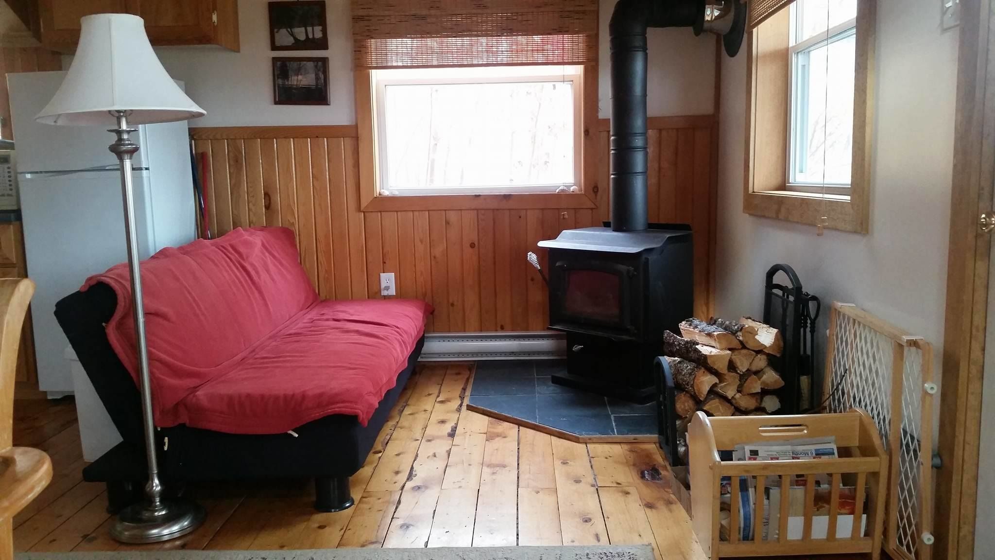 Une pièce chaleureuse avec un canapé rouge, une lampe, une cheminée et une fenêtre.