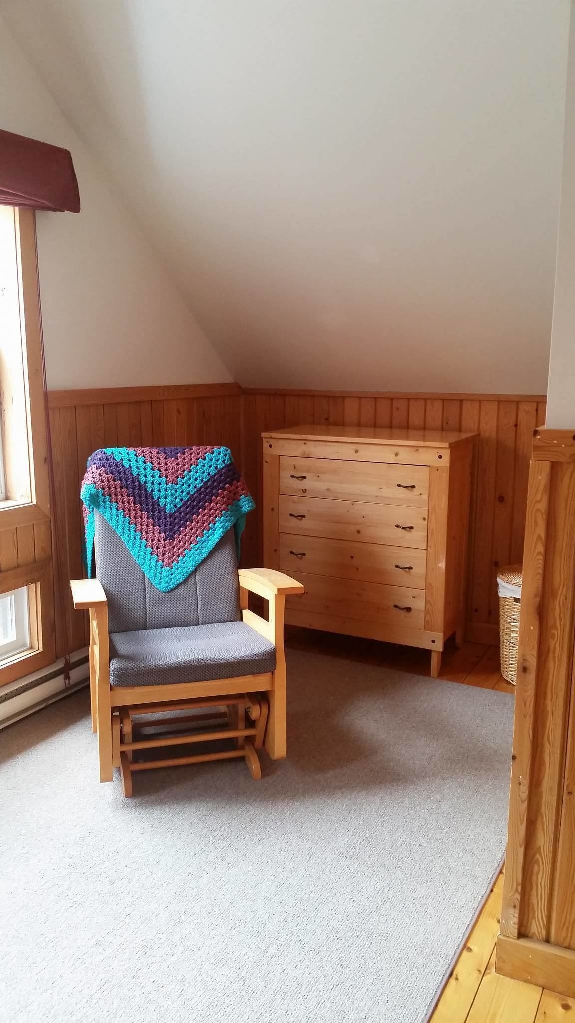 A corner room with a wooden chair, a wooden dresser, and a window.