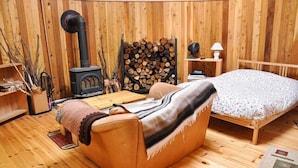 Una habitación acogedora con detalles de madera, un sofá, una cama, una chimenea y leña apilada.