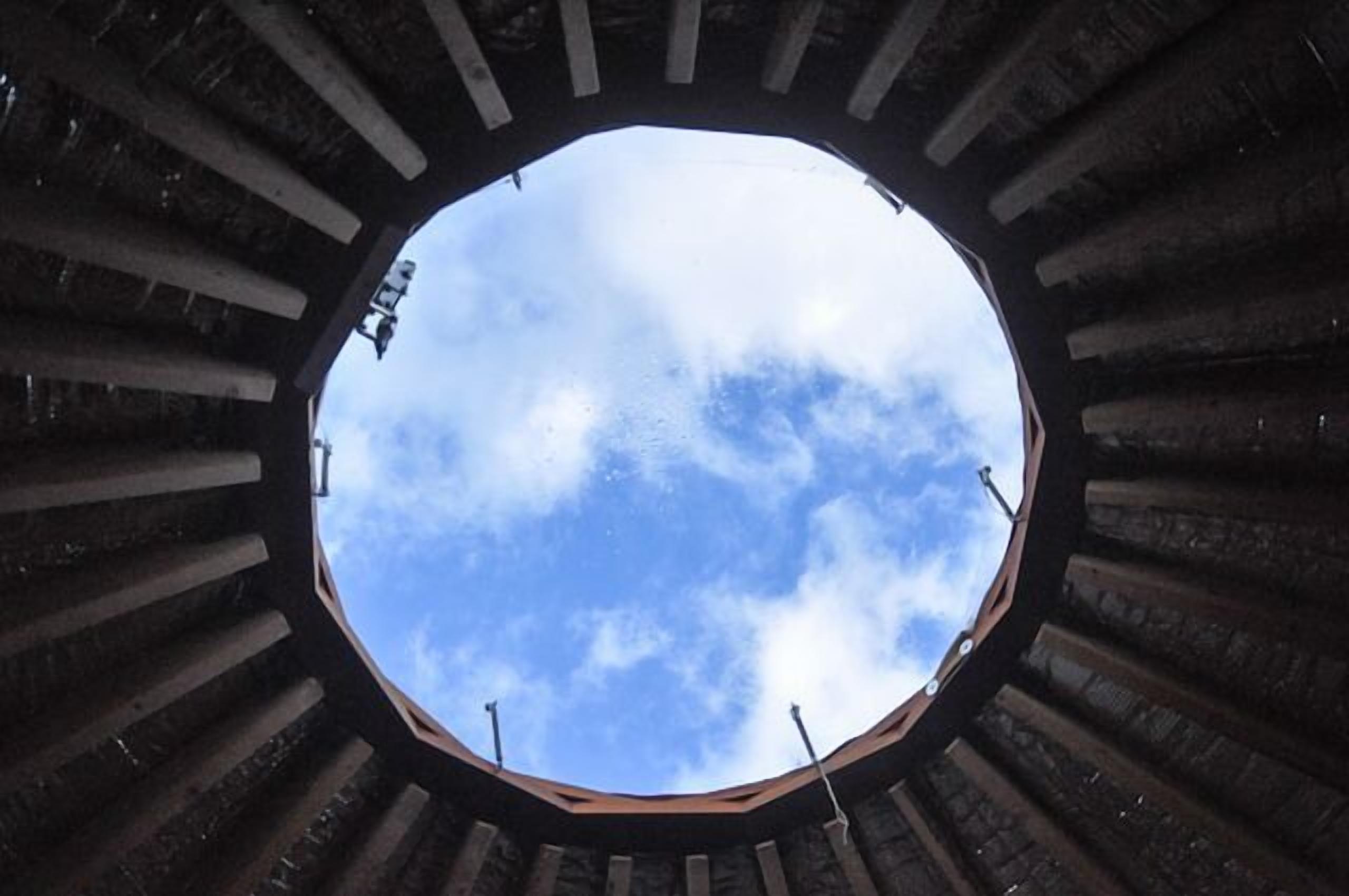 A circular window with a view of the sky through a structure with vertical beams.
