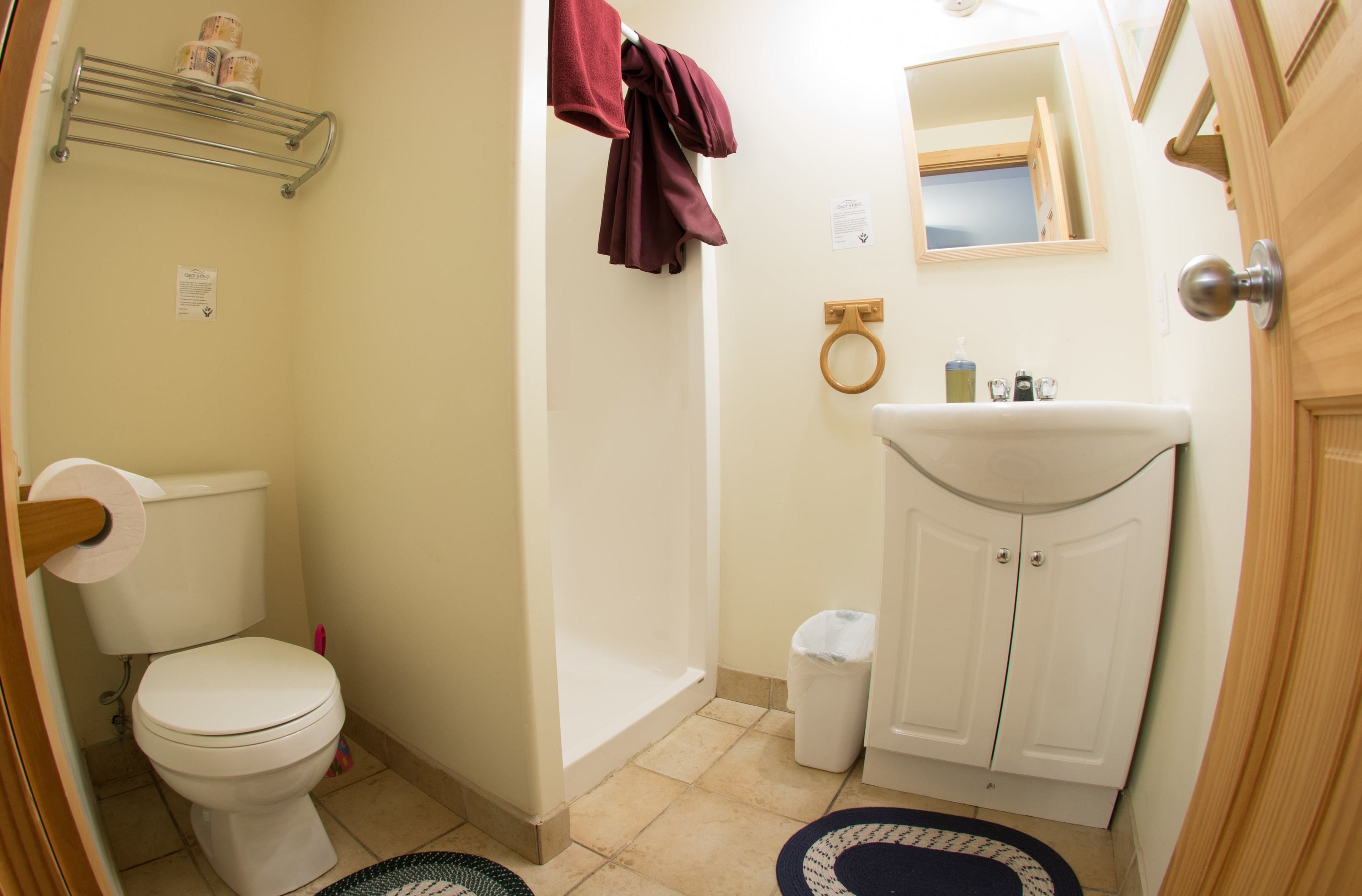 A bathroom with a toilet, sink, and shower. There is a towel rack with towels and a mirror above the sink.