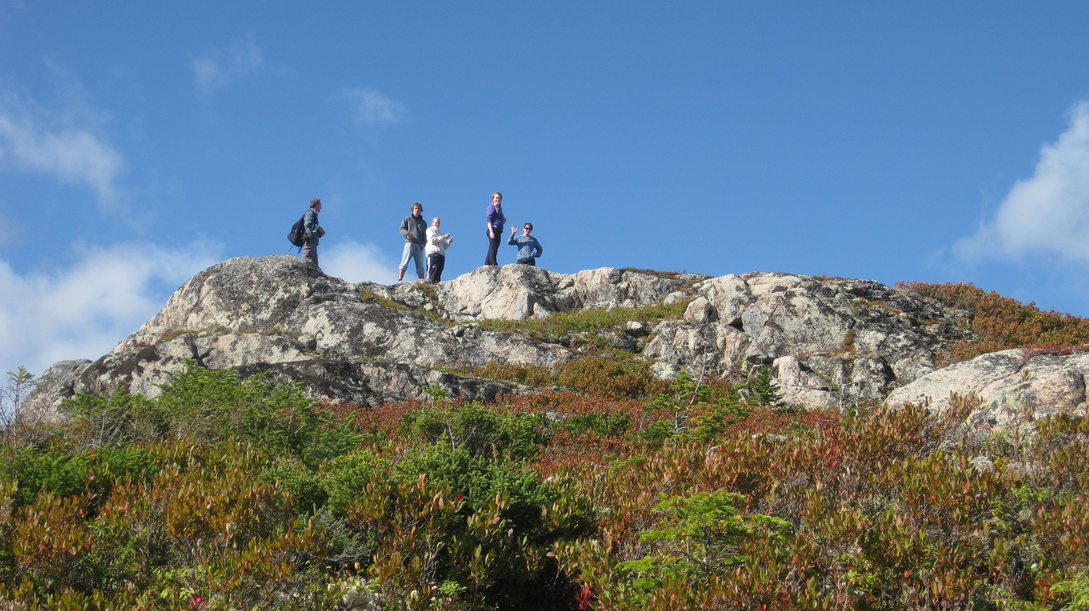 A group of people standing on a rocky hilltop with sparse vegetation.