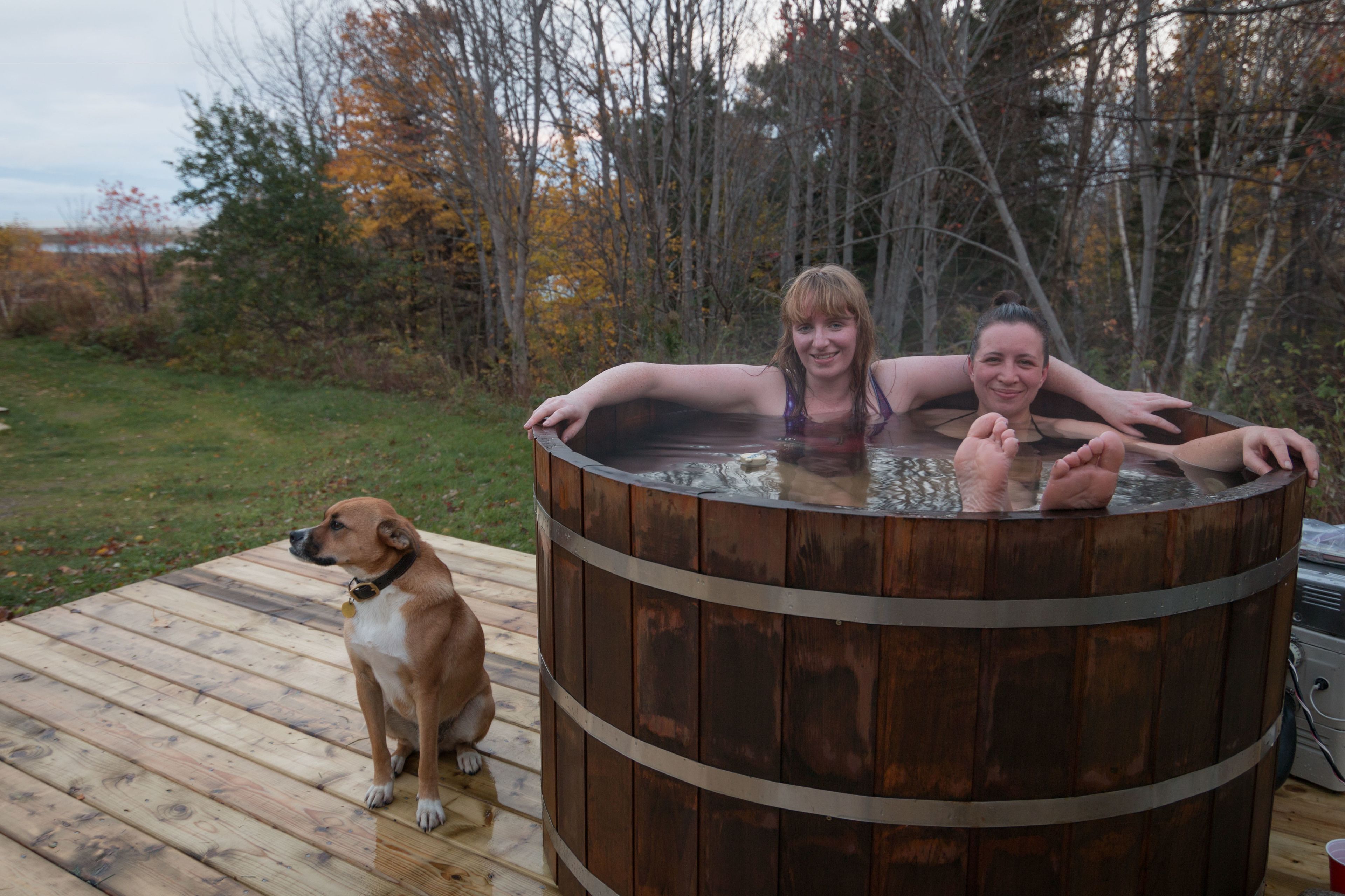 A wooden hot tub on a deck with a dog nearby.