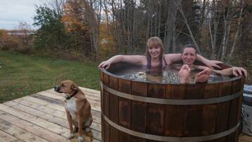 A wooden hot tub on a deck with a dog nearby.