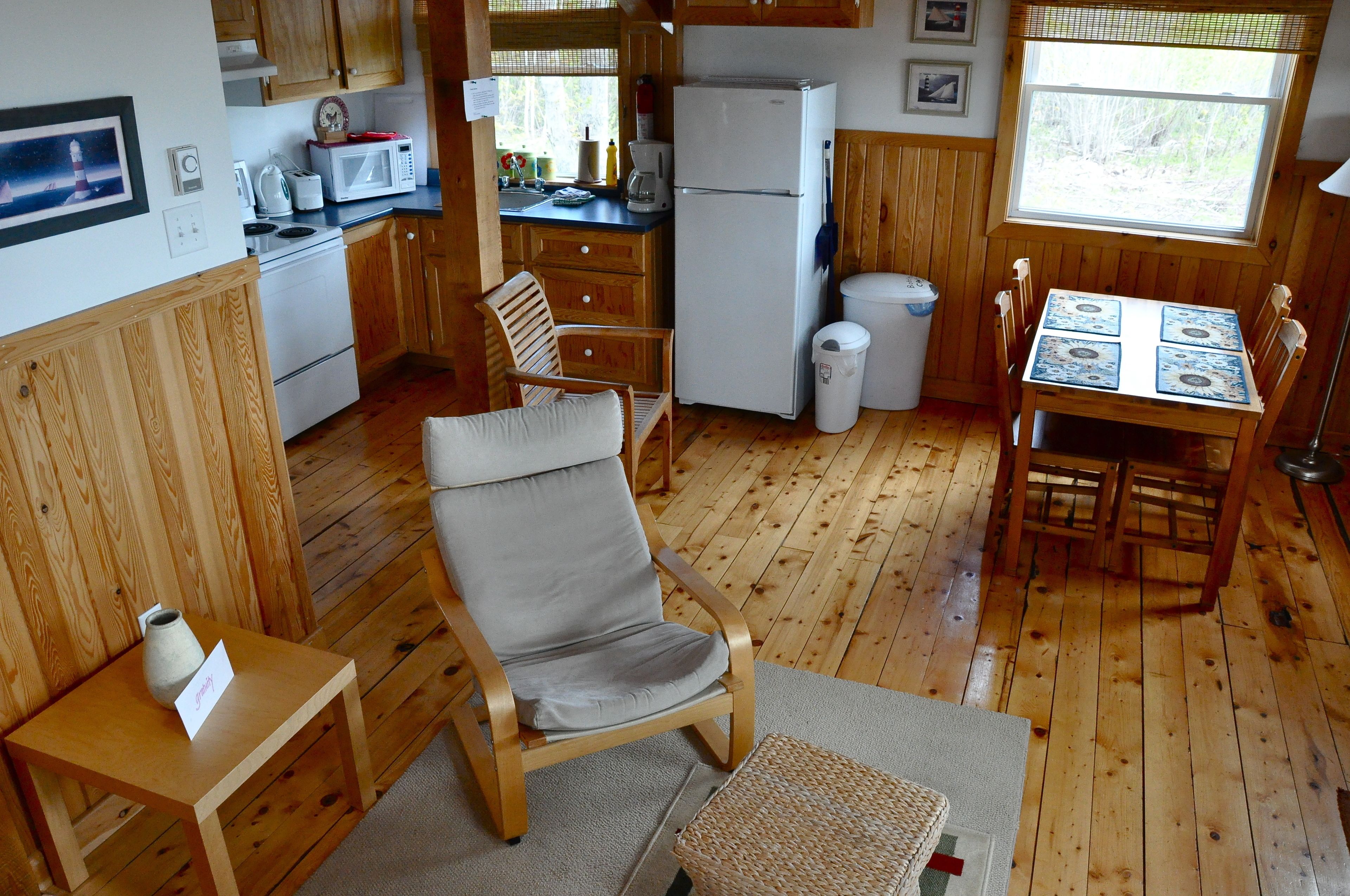 A wooden-floored kitchen with a dining table, chairs, a refrigerator, a microwave, and a sink.