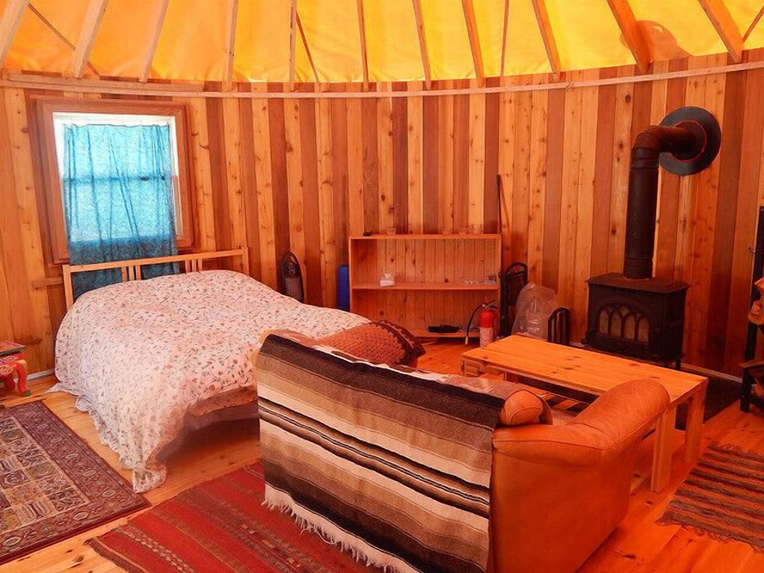 Ein gemütliches Zimmer mit einem Bett, einem Schlafsofa, einem Tisch, einem Bücherregal und einem Kaminofen.