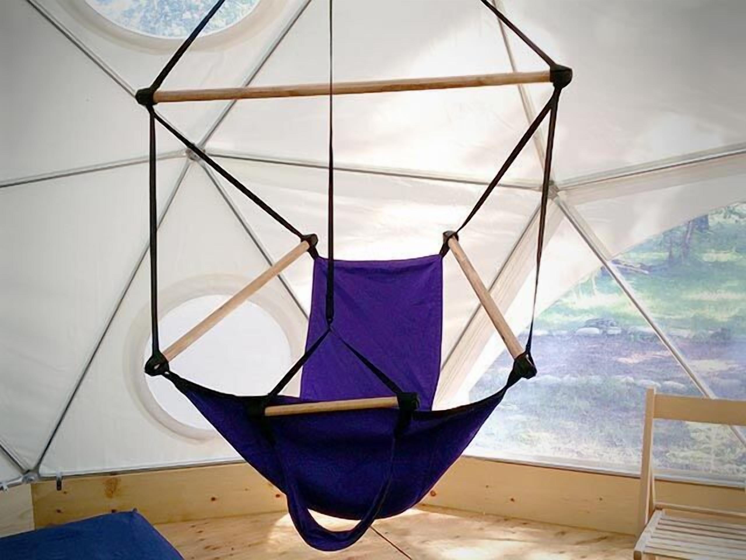 A hanging chair suspended from a tent's ceiling, with a view of a forest through the window.