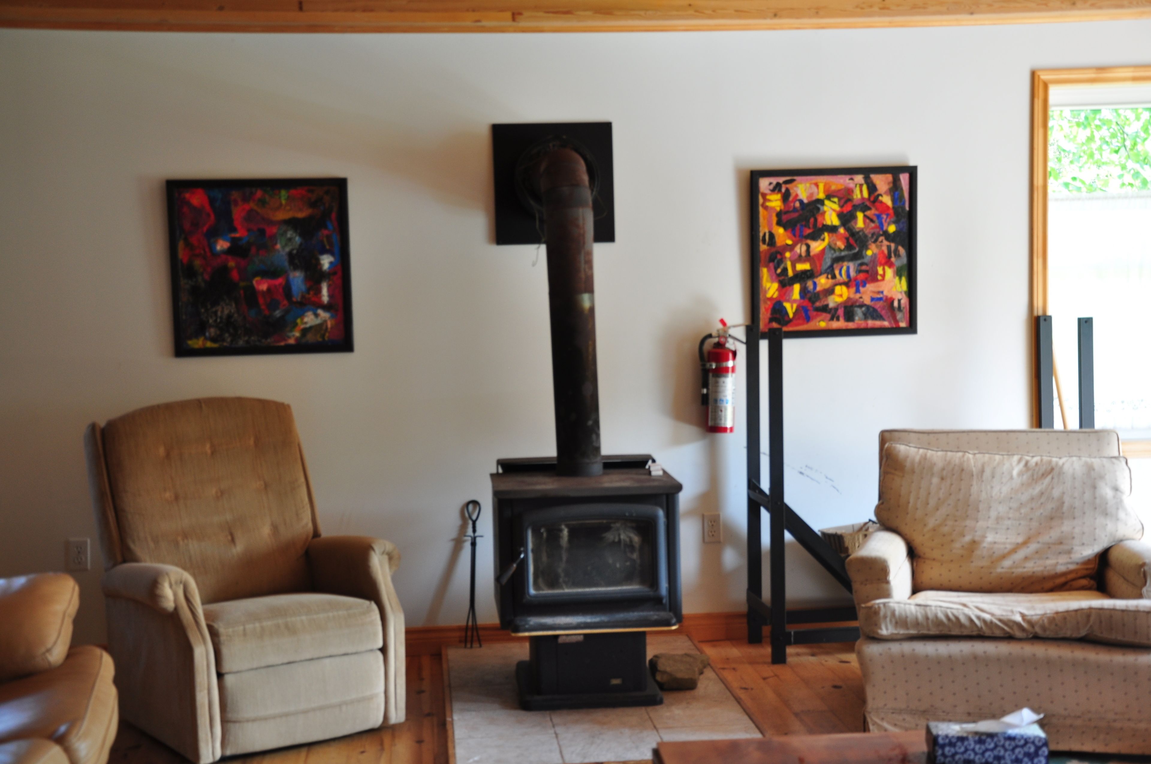 A living room with a wood-burning stove, two armchairs, and abstract paintings on the walls.