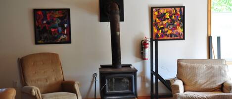 A living room with a wood-burning stove, two armchairs, and abstract paintings on the walls.