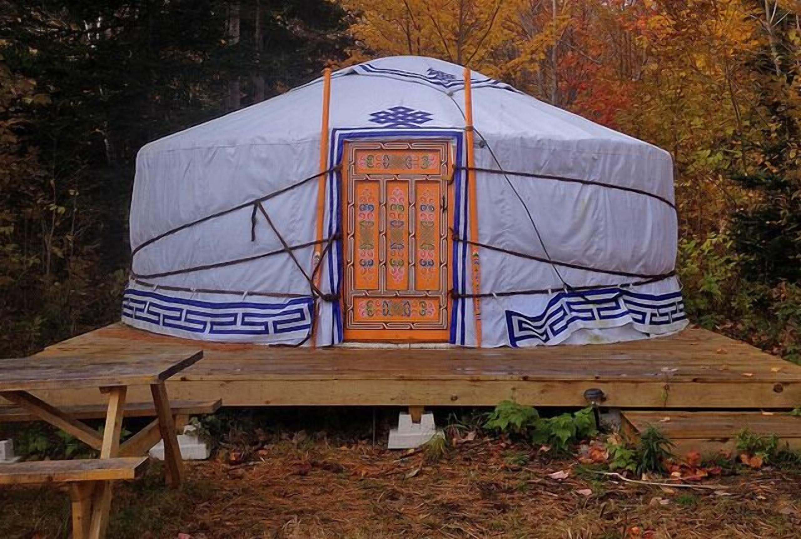 A traditional yurt with a decorative door, set on a wooden platform in a forested area.