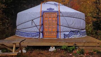 A traditional yurt with a decorative door, set on a wooden platform in a forested area.