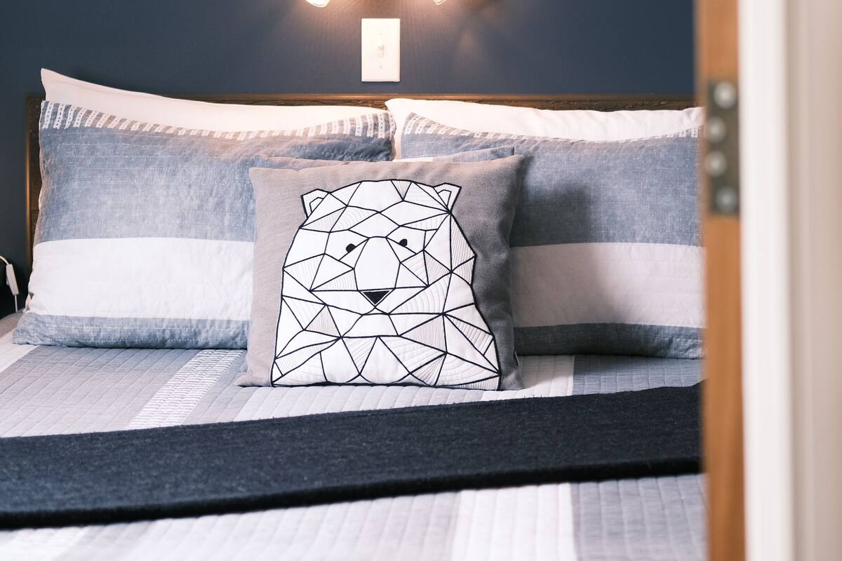 A neatly made bed with striped bedding and a geometric pillow design.
