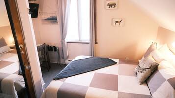 A bedroom with two beds, a window with curtains, a small table, and a wall-mounted picture.