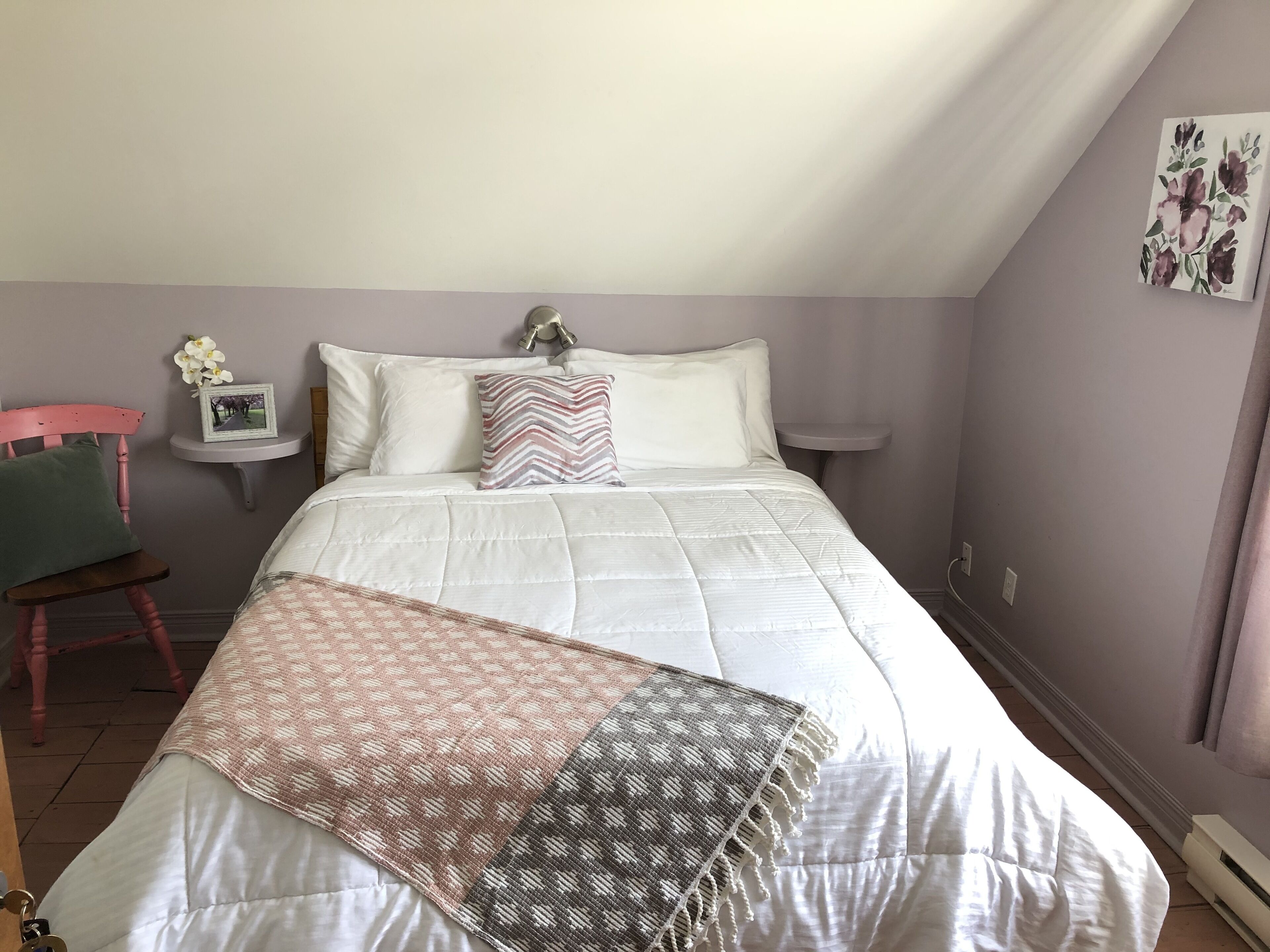 Quarto com cama, mesa de cabeceira, cadeira e um quadro na parede.