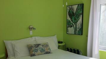 Een slaapkamer met een bed, een plafondventilator, een groene wand, een raam met gordijnen en een aan de wand bevestigde plant.
