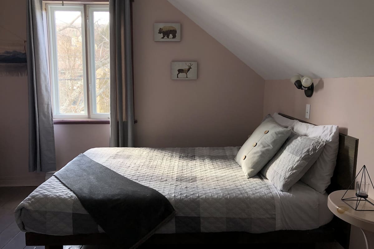 A bedroom with a bed, a window with curtains, and two wall-mounted pictures.