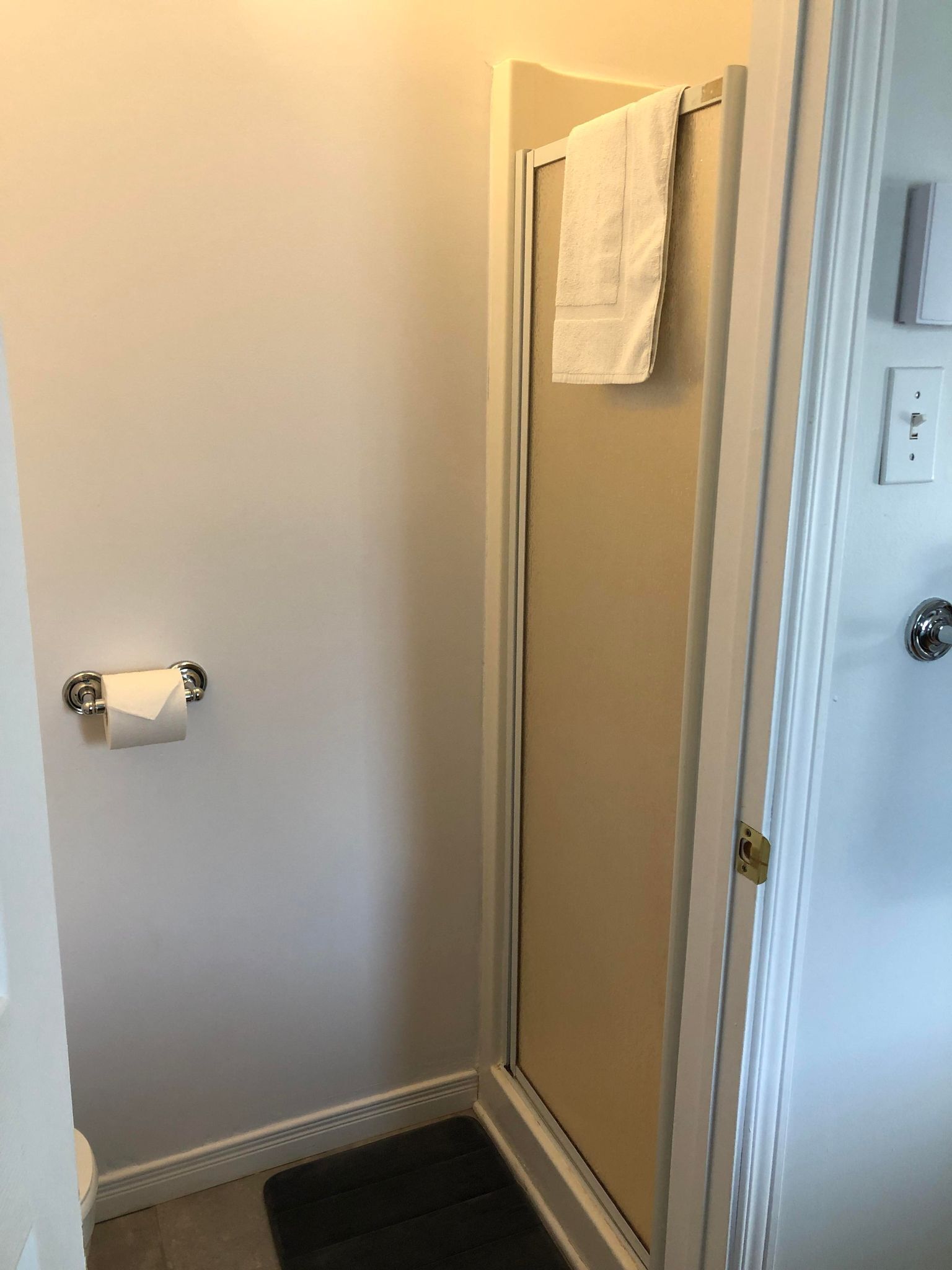 A bathroom with a glass shower door, a towel hanging on the door, and a toilet paper holder.