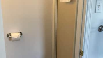 A bathroom with a glass shower door, a towel hanging on the door, and a toilet paper holder.