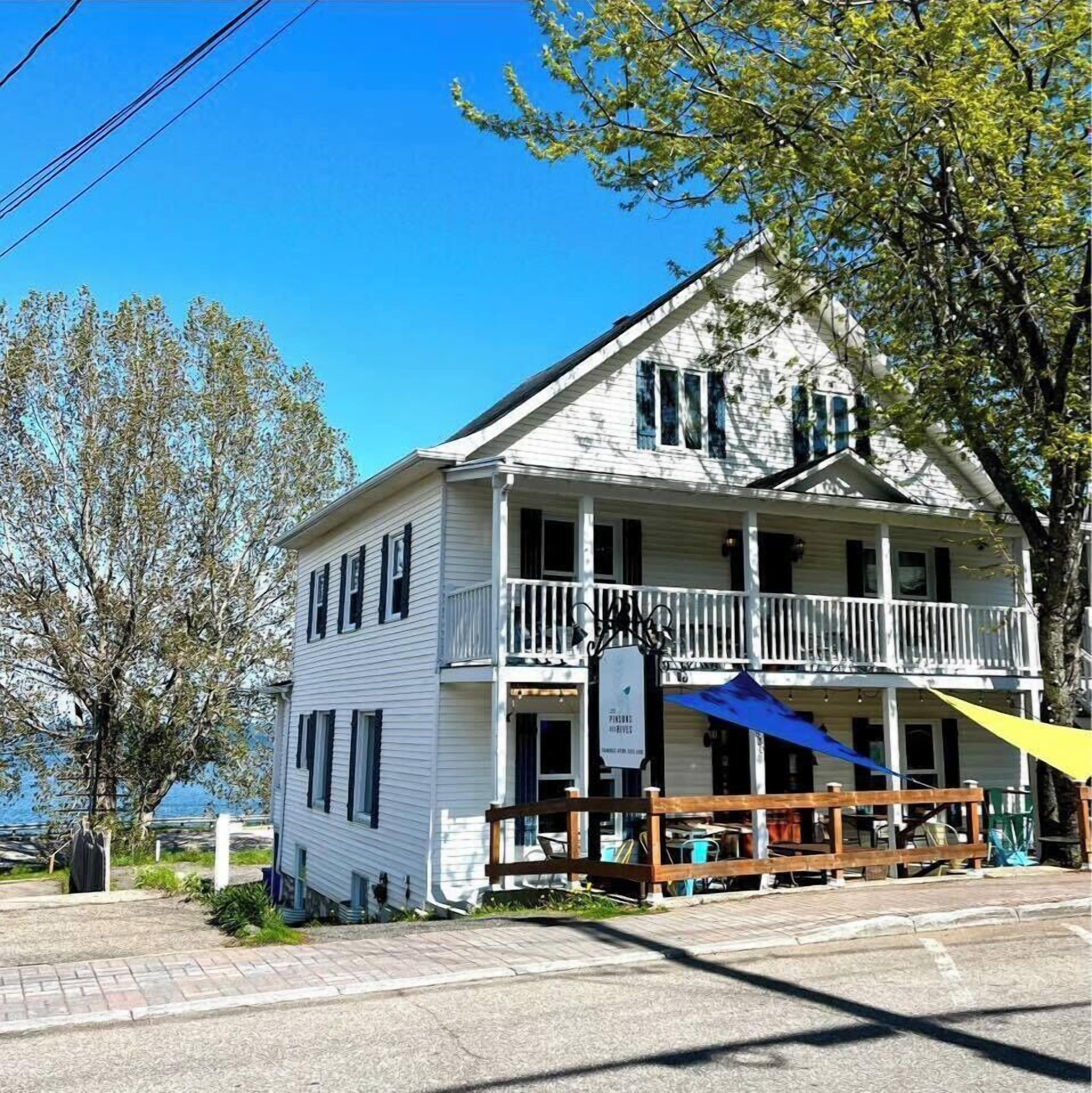 A two-story white building with a balcony, a covered porch, and a sign indicating a business.