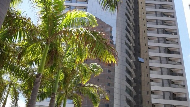 A tall building with a modern architectural design, featuring a series of balconies and a reflective glass facade. - Betel Beach Class Internacional (Recife)