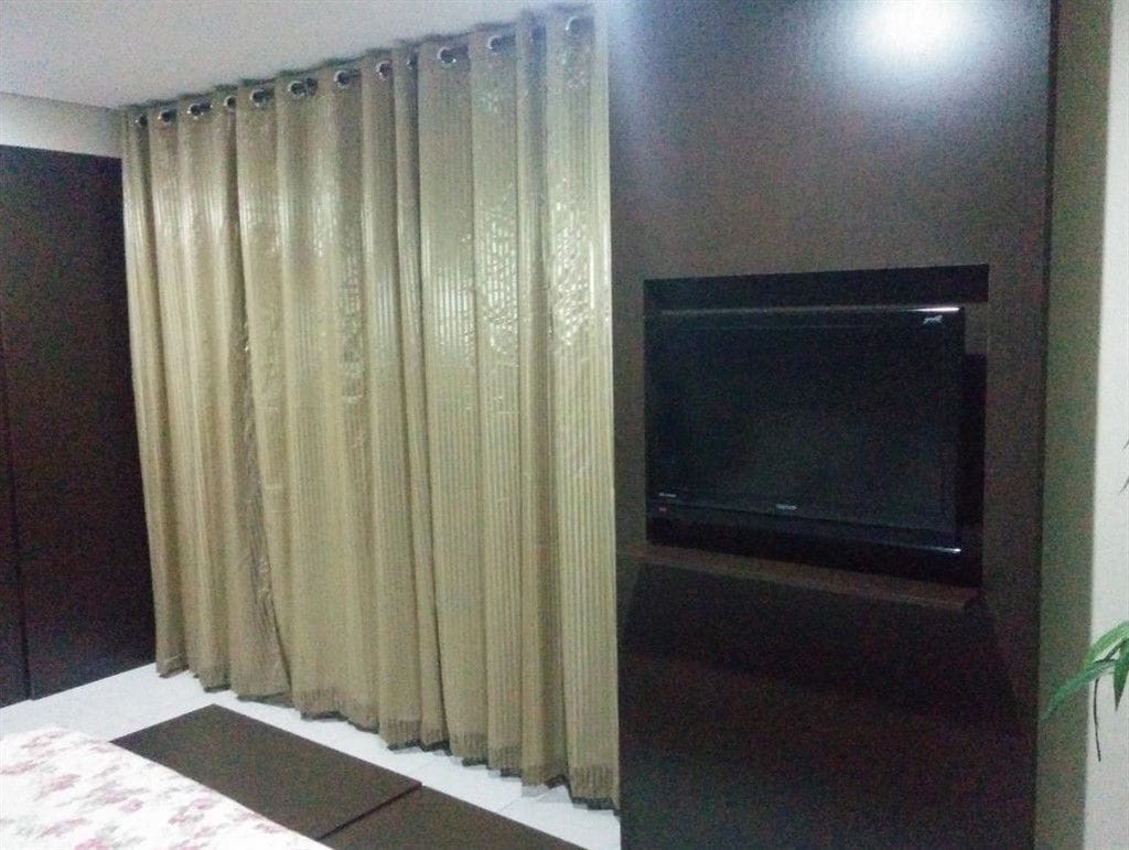 A room with a bed, a TV mounted on the wall, and a curtain covering the window.