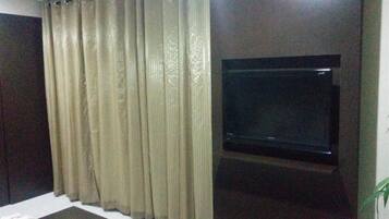 A room with a bed, a TV mounted on the wall, and a curtain covering the window.