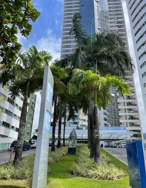 A modern building with a glass facade, surrounded by palm trees and a well-maintained lawn. - Betel Beach Class Internacional (Recife)